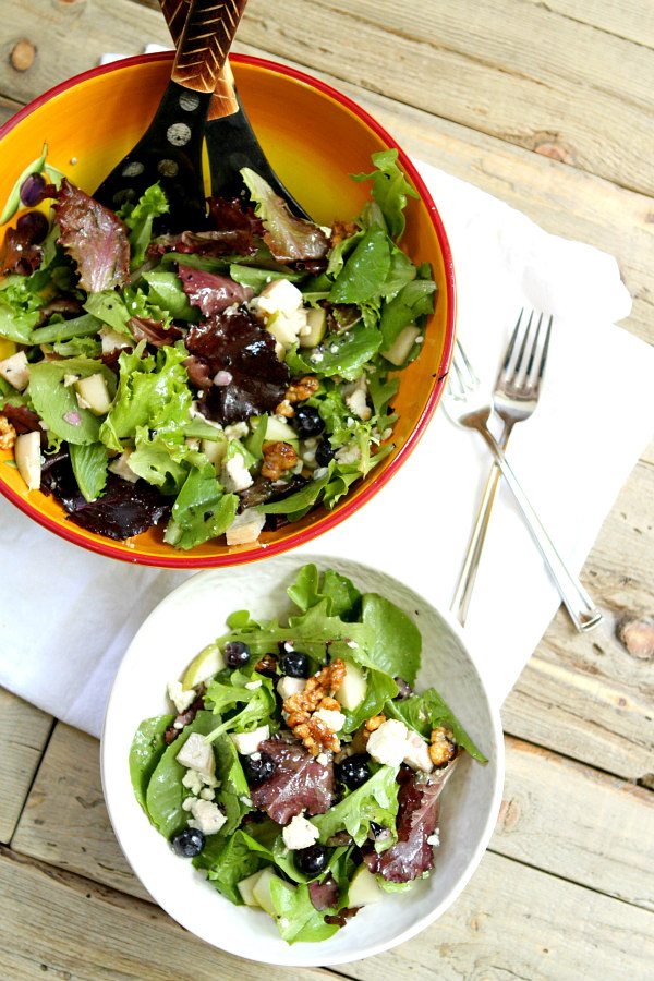 Blueberry, Bleu and Glazed Walnut Salad in a yellow bowl with salad servers. separate white bowl with a serving of the salad in it and two forks on the side, set on a white towel