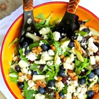 blueberry, blue cheese and glazed walnut salad in a yellow bowl with salad servers
