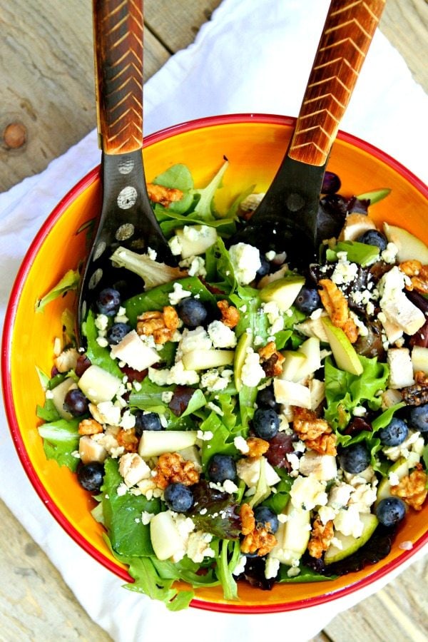 Blueberry, Blue Cheese and Glazed Walnut Salad in a yellow salad bowl with wooden salad servers, sitting on a white towel on a wooden table