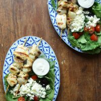 greek chicken kebabs plated with greek salad and sauce