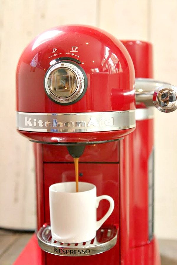 Red KitchenAid Nespresso machine brewing a cup of espresso in a white cup