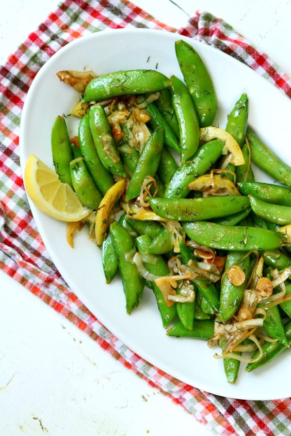 Lemony Stir Fried Sugar Snap Peas on a white serving platter on top of an orange/green/white checked napkin