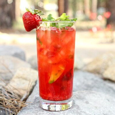strawberry mojito in a tall glass garnished with a fresh strawberry sitting on rocks in a backyard setting