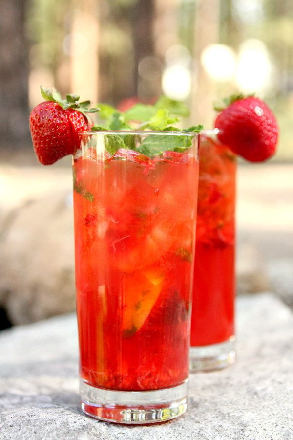 two Strawberry Mojitos garnished with fresh strawberries sitting on a rock