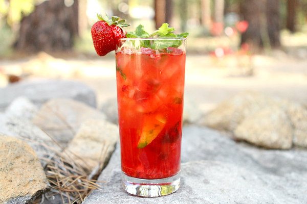 Strawberry Mojito in a tall glass garnished with a fresh strawberry set on rocks in a backyard setting