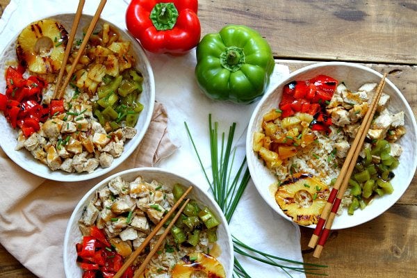 overhead shot of 3Grilled Chicken and Pineapple Rice Bowls with Teriyaki Glaze in white bowls with chopsticks. bell peppers and chives displayed for garnish