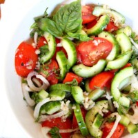 Overhead shot of Tomato Cucumber and Basil Salad in a white bowl with a white napkin on a wood surface