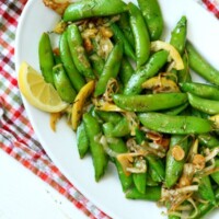 lemony stir fried sugar snap peas on a white serving platter set on a checked cloth napkin