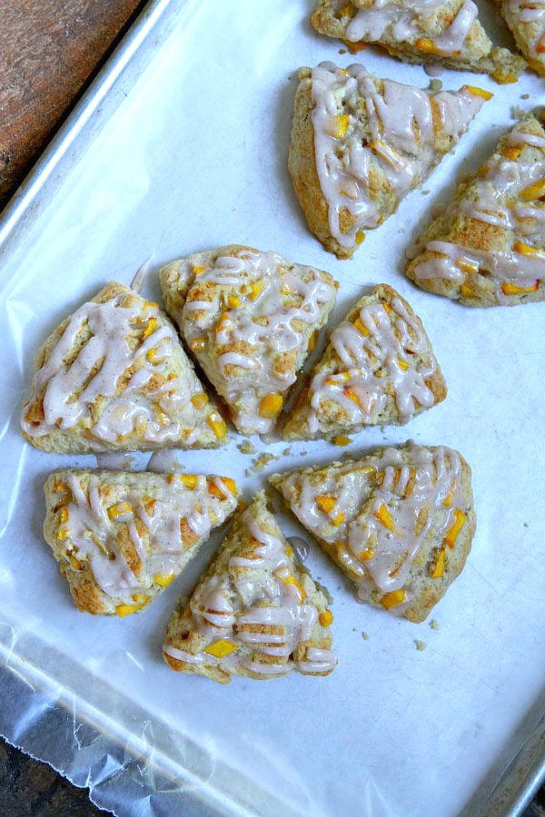 overhead shot of fresh peach scones drizzled with glaze. Set on a white platter