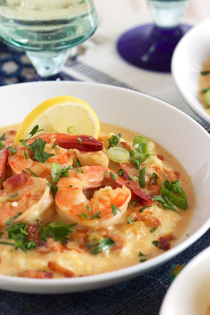 shrimp and grits in a white bowl garnished with a lemon slice and served with wine