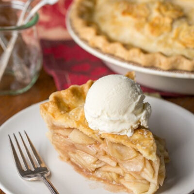 slice of apple pie on a plate with rest of pie in background