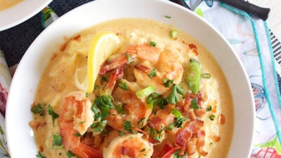 overhead shot of shrimp and grits in a white bowl on a patterned napkin with a fork and two other partial views of shrimp and grits bowls