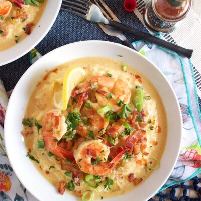 overhead shot of shrimp and grits in a white bowl on a patterned napkin with a fork and two other partial views of shrimp and grits bowls