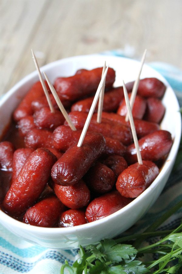 Lil Smokies Appetizer in a white bowl with toothpicks. Set on a blue striped napkin with fresh parsley on the side.