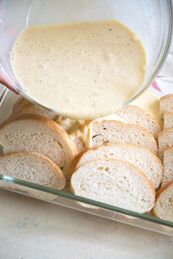 Pouring custard on Eggnog French Toast Casserole in a casserole dish