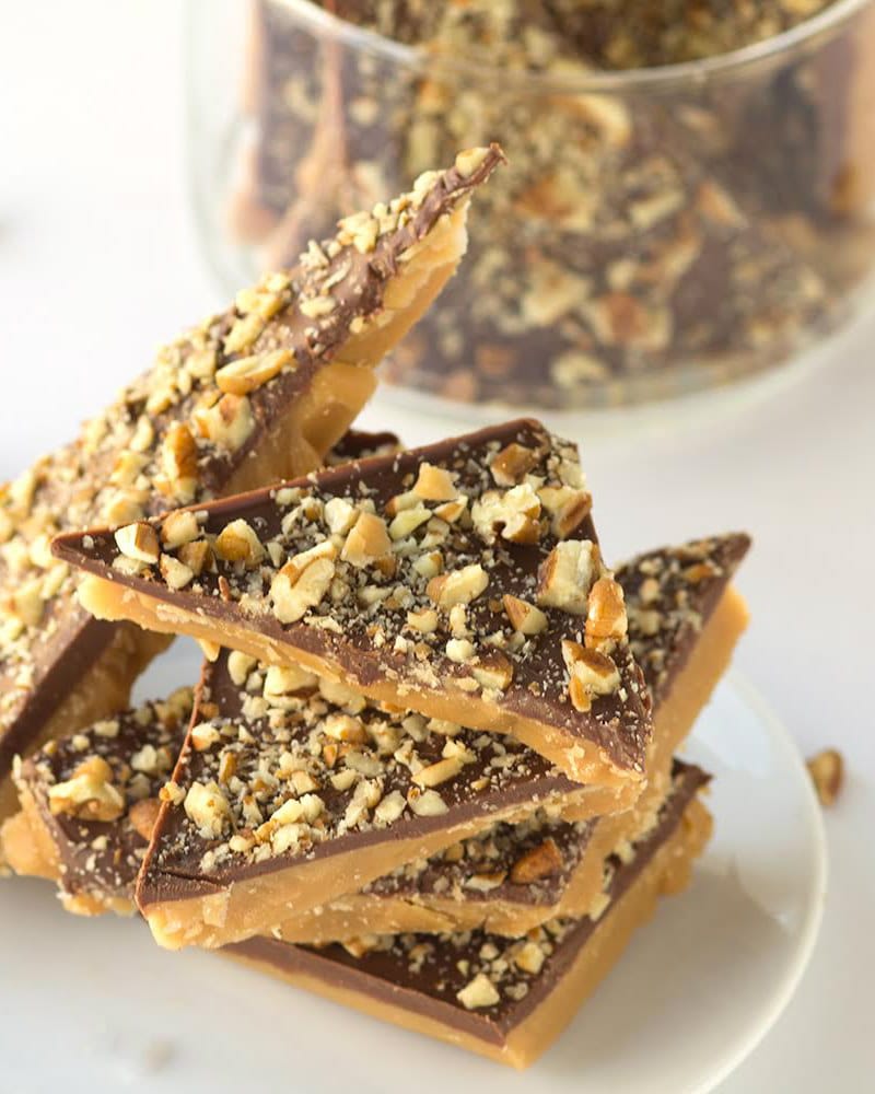 Heath Bars stacked on a white plate with a glass bowl of more heath bar pieces in the background