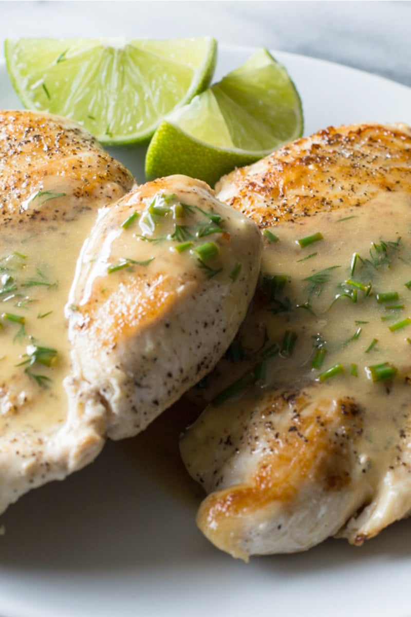 atwo chicken breasts topped with lime butter and garnished with lime wedges on a white plate