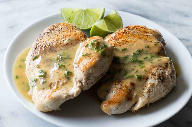 two chicken breasts topped with lime butter on a white plate with lime wedges