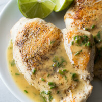 chicken topped with lime butter on a white plate with fresh lime wedges