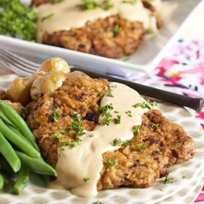 chicken fried steak with gravy on top and fresh green beans. Displayed on a polka dot stack of plates.
