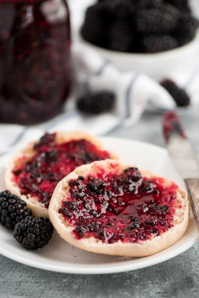 Blackberry Freezer Jam spread on English muffins on a white plate with fresh blackberries