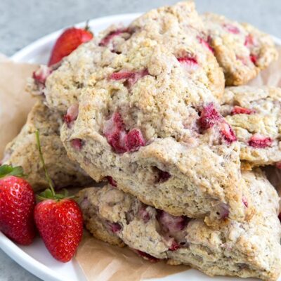 strawberry buttermilk scones stacked on a white plate with a few fresh strawberries