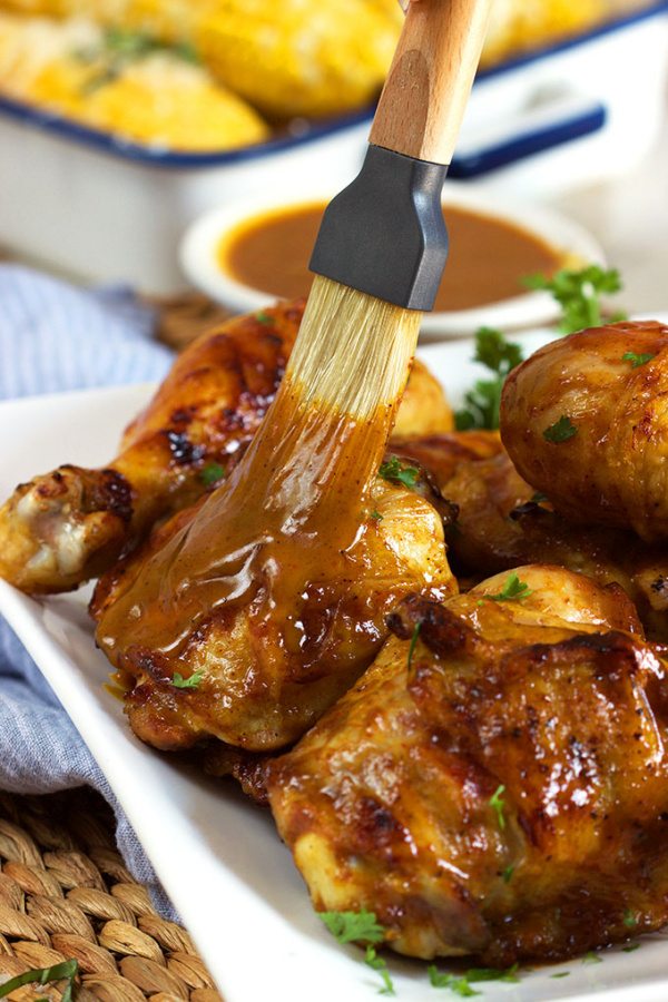 Carolina Style Barbecue Chicken on a white serving platter with a brush brushing sauce onto it. bowl of sauce in background and corn on the cob