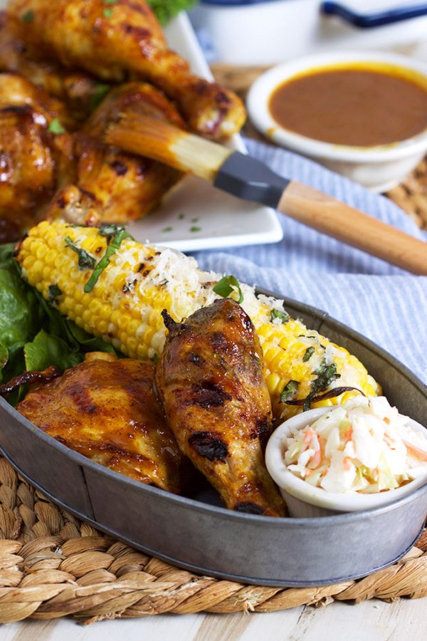 Carolina Style Barbecue Chicken in a metal serving dish with corn on the cob and cole slaw with more chicken and sauce and a brush in the background