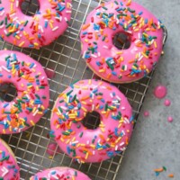 pink glazed doughnuts with rainbow sprinkles on a cooling rack