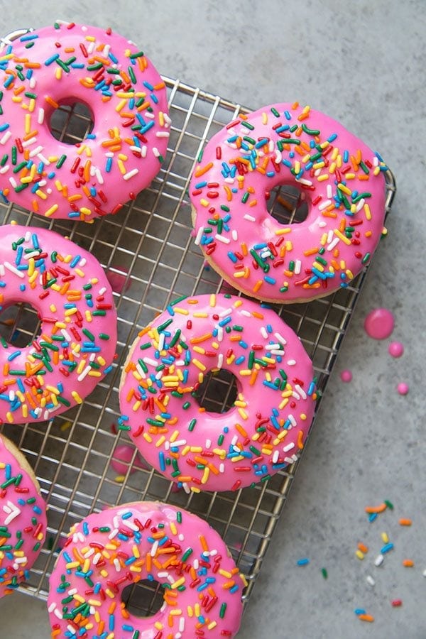 pink glazed doughnuts with rainbow sprinkles on a cooling rack