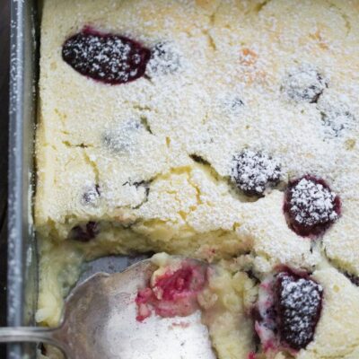 blackberry lemon pudding cake in a metal pan with a serving spoon spooning some of the cake out of the pan