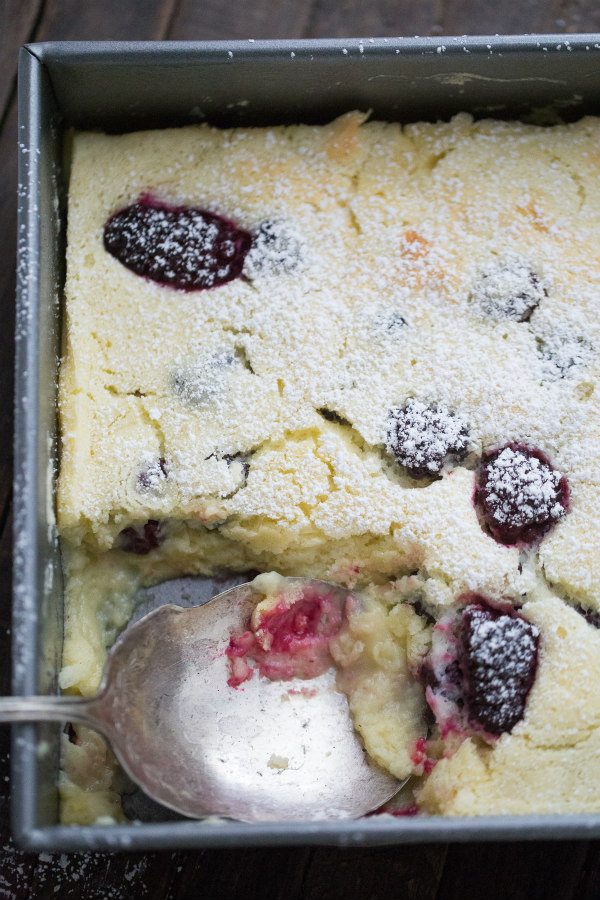 blackberry lemon pudding cake in a metal pan with a serving spoon spooning some of the cake out of the pan