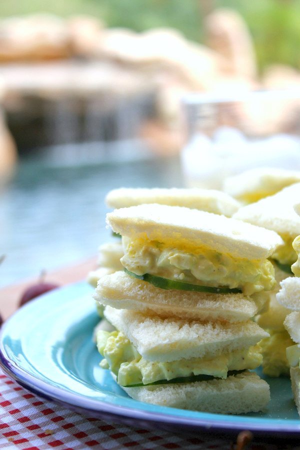 Avocado Egg Salad Tea Sandwiches stacked on a blue plate set on a white/red checked napkin