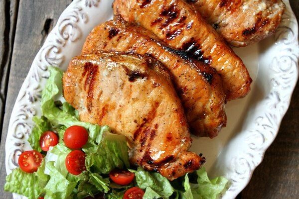 Blue Cheese and Apple Stuffed Grilled Pork Chops displayed on a white platter with lettuce/tomato salad