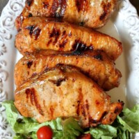 apple and blue cheese stuffed grilled pork chops on a white serving platter with lettuce and tomato salad