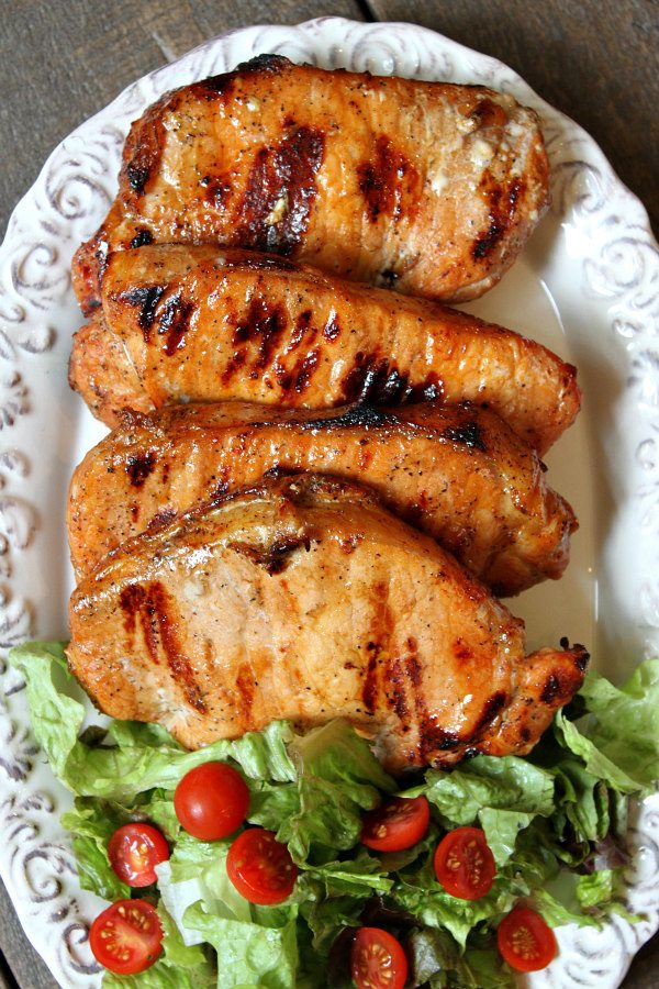 Blue Cheese and Apple Stuffed Grilled Pork Chops displayed on a white platter with a lettuce and tomato salad