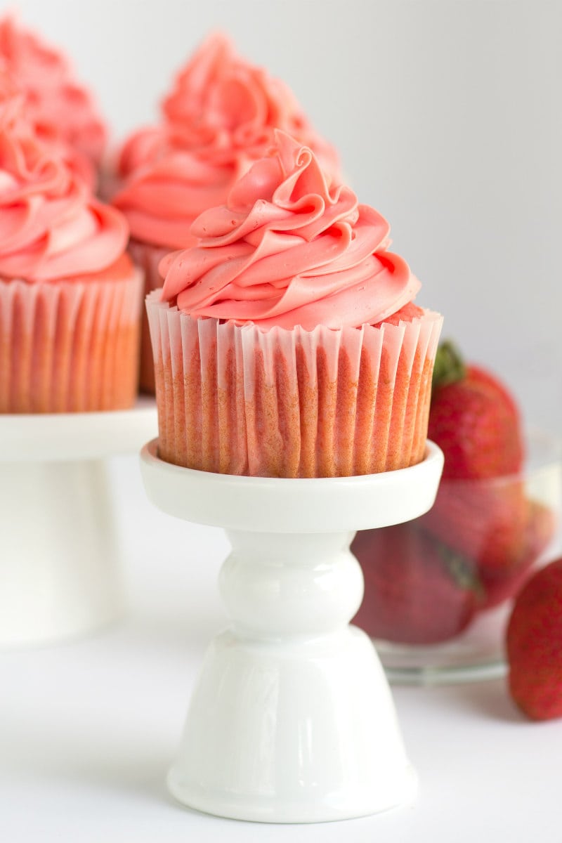 pink strawberry cupcakes on white cupcake stands with fresh strawberries in the background