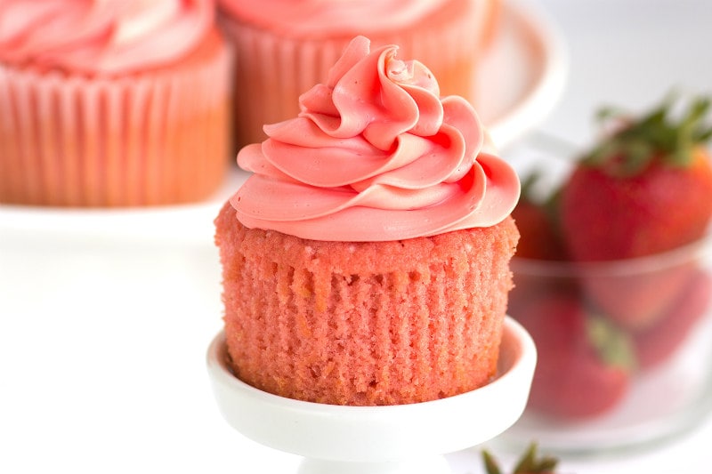pink strawberry cupcake on a white cupcake stand unwrapped with fresh strawberries on the side