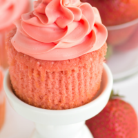 pink strawberry cupcake on a white cupcake stand unwrapped with fresh strawberries on the side