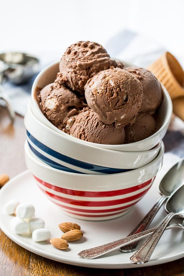 several scoops of Rocky Road Ice Cream in a white and blue/red striped dish stacked on top of more dishes. spoons, marshmallows and almonds on side