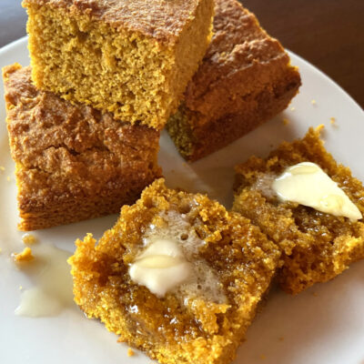 pumpkin cornbread on a white plate sliced with butter