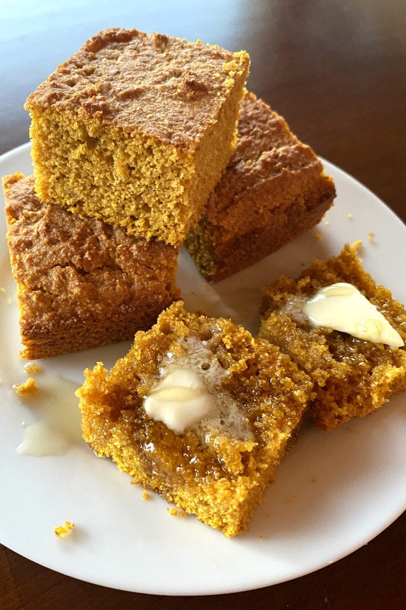 pumpkin cornbread on a white plate sliced with butter