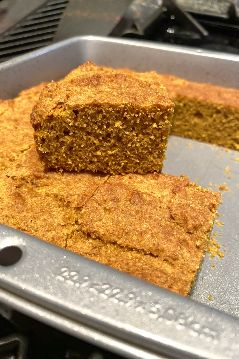 pumpkin cornbread in a baking pan with slice on top