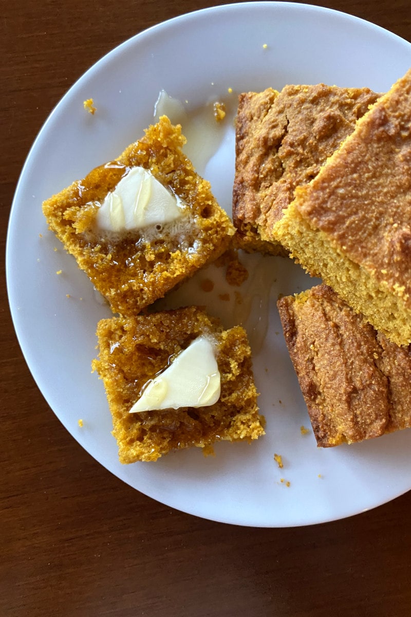 pumpkin cornbread on a white plate sliced with butter
