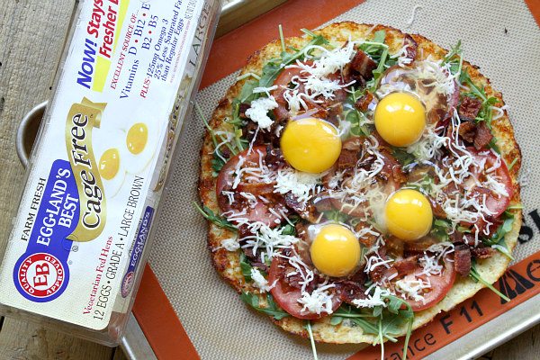 preparing Cauliflower Crust Bacon and Egg Pizza adding eggs