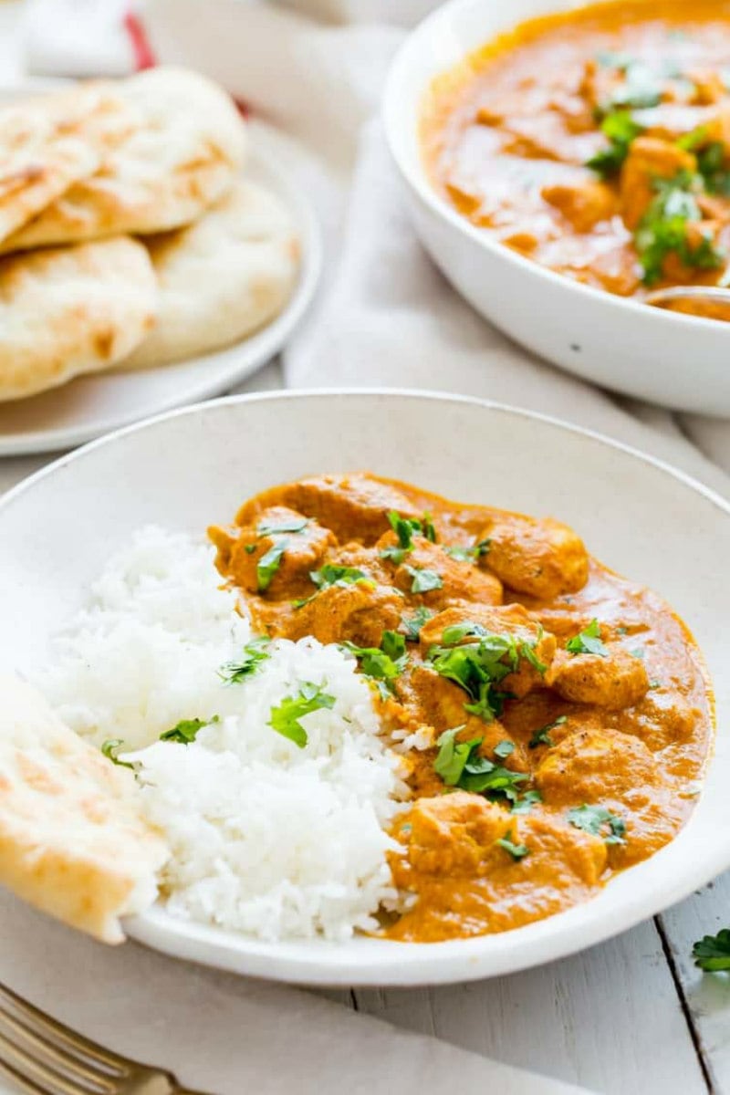 servings of indian butter chicken in white bowls with white rice with pita bread in the background