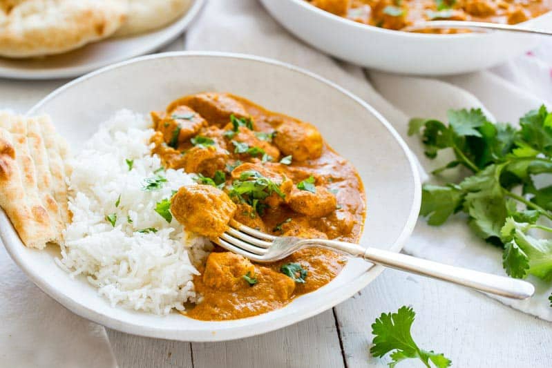 serving of indian butter chicken and white rice in a white bowl with a forkful of chicken and cilantro garnish