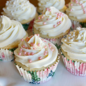 wedding cupcakes with white buttercream and pink pearls on a white cake platter