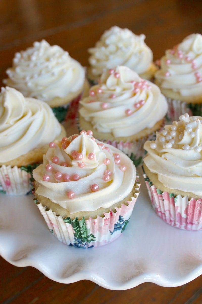 wedding cupcakes with white buttercream and pink pearls on a white cake platter