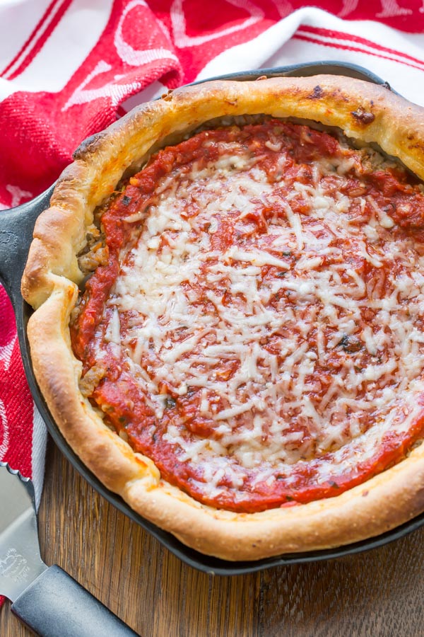 overhead shot of chicago style deep dish pizza displayed on a wooden board with a red print cloth napkin